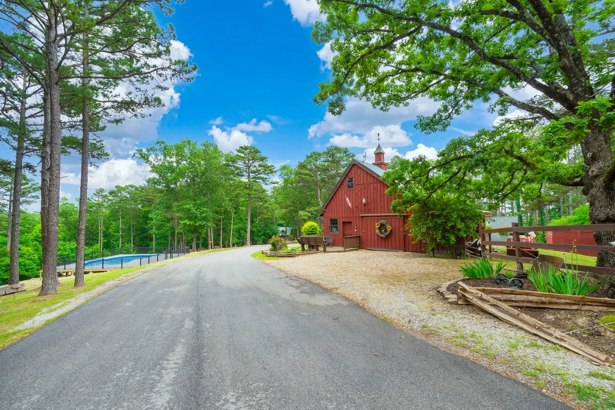 The vibrant exterior scene includes a classic red barn, a sprawling tree, a driveway, and a swimming pool, all set against lush greenery. The image captures a variety of outdoor spaces perfect for recreation and relaxation.
