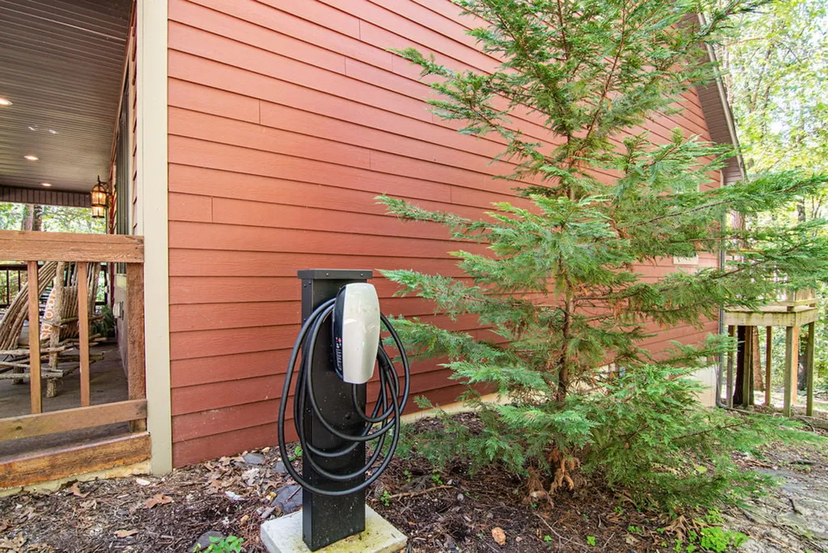 An electric vehicle charging station set beside a wooden deck and a green tree, blending eco-friendly convenience with natural surroundings. The peaceful scene invites relaxation while charging up for new adventures.