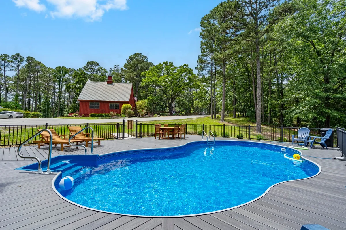 An inviting saltwater swimming pool with a red house in the background, surrounded by deck chairs and lush greenery. The tranquil outdoor setting is ideal for swimming, sunbathing, and poolside gatherings.