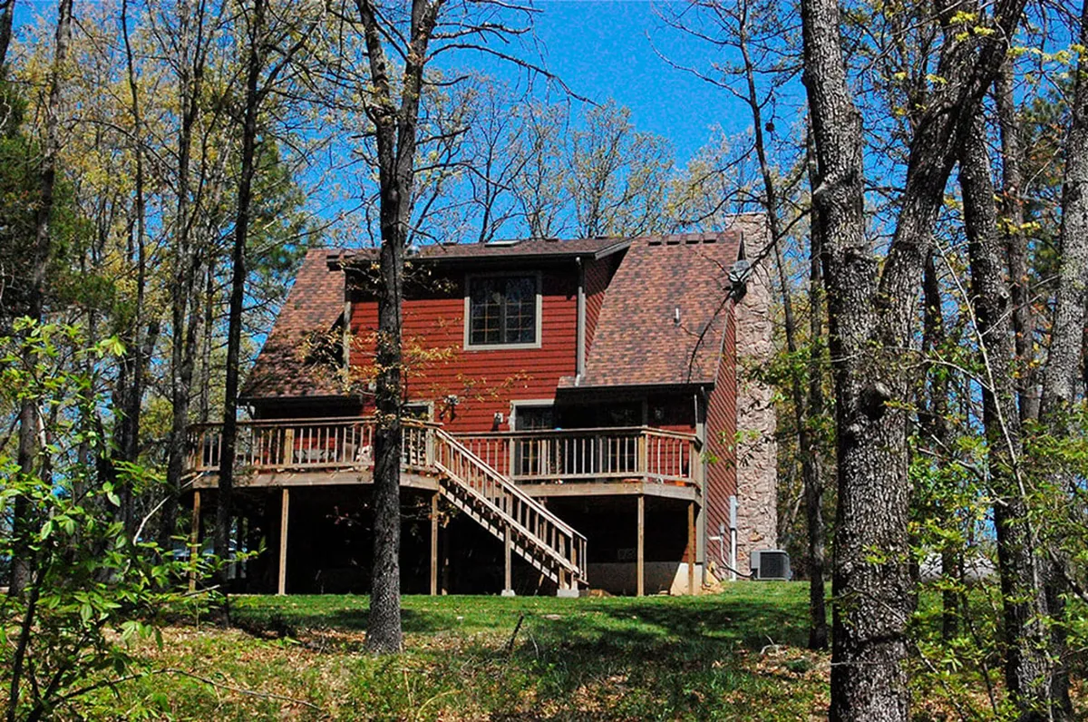 A wooden deck with a warm red exterior is nestled among tall trees. The deck offers a peaceful spot to relax outdoors, surrounded by nature's sights and sounds. The seclusion is palpable, with no neighboring structures in sight, and the setting is alive with possibilities for wildlife encounters or quiet reflection.