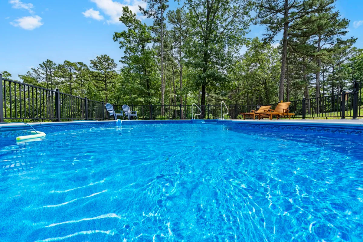 An exterior view of a swimming pool with lounge chairs, set amidst surrounding trees. The scene is bright and inviting, suggesting opportunities for midday swims and outdoor leisure.