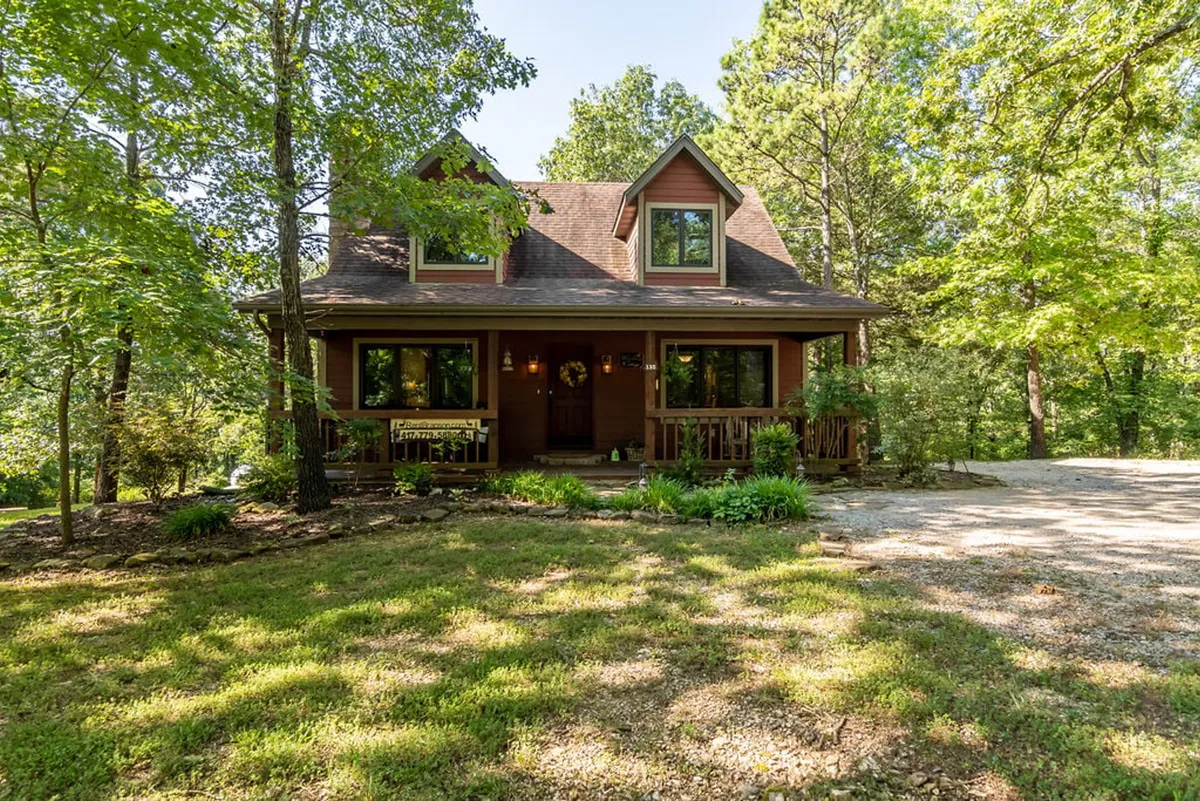 This image showcases the front porch of Woodsong Cottage, featuring large windows and natural landscaping. The setting is surrounded by trees, creating a sense of tranquility and seamless connection with nature.