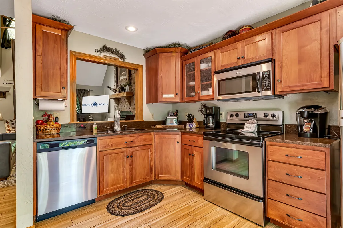 A chef-inspired kitchen featuring wooden cabinetry, gleaming stainless steel appliances, granite-look countertops, and elegant decor. The kitchen is bathed in natural light, with a window offering views of the outdoors. The space is arranged for both cooking and entertaining, promoting a seamless flow between kitchen and living areas.