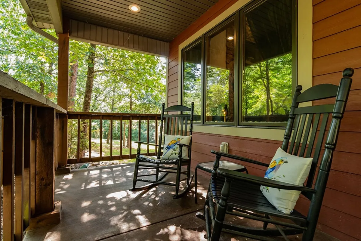 This image features an exterior view with rocking chairs set on a porch, decorative pillows adding comfort, and lush greenery in the background. The setting is peaceful and inviting, suggesting a tranquil environment perfect for unwinding.
